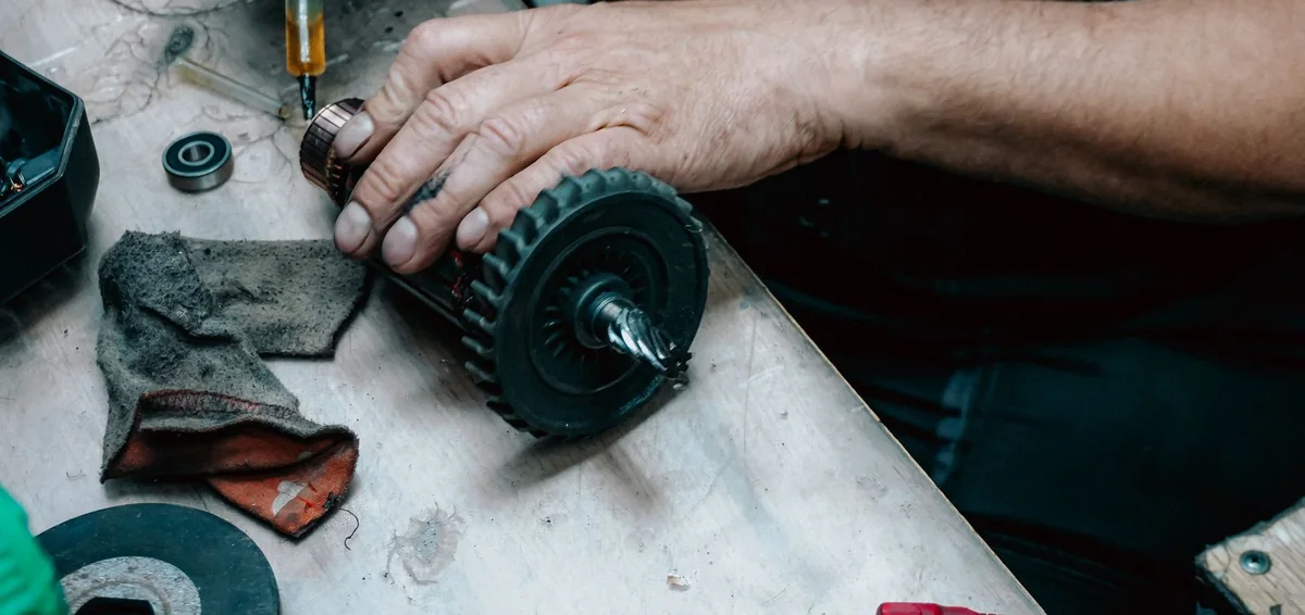 Montaż i demontaż łożysk: dłoń mechanika trzymająca wirnik elektronarzędzia, na stole leży łożysko kulkowe z uszczelnieniami
